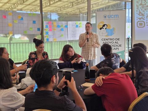 Una charla educativa donde un expositor se dirige a un grupo atento de jóvenes en un ambiente colaborativo.