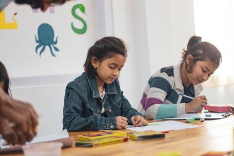 Dos niñas están dibujando en una mesa con materiales de arte.