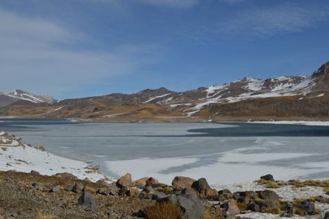 Una vista panorámica de un lago helado rodeado de montañas y vegetación escasa.