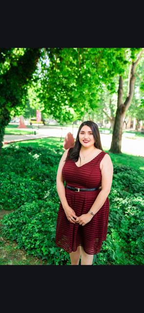 Una mujer sonriente con un vestido burdeos posando en un parque verde.