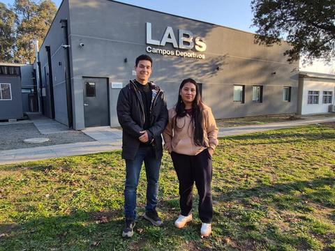 En la imagen se ven dos jóvenes posando frente a un edificio que dice LABS Campos Deportivos.