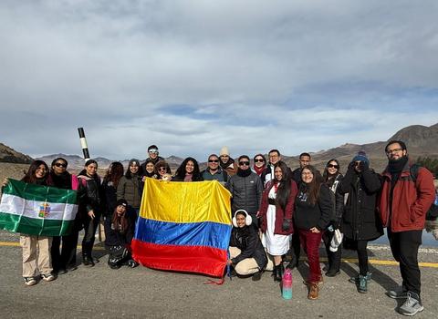 Un grupo de personas posando con banderas de Colombia y otra bandera, en un paisaje montañoso.