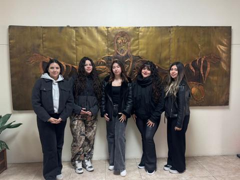 Un grupo de cinco amigas posan alegremente frente a una pintura significativa en la pared.