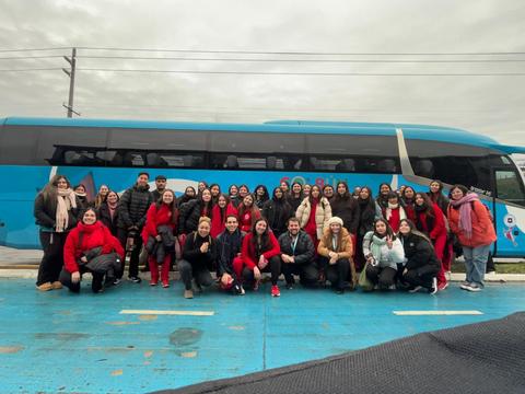 Un grupo grande de personas vestidas de rojo posando frente a un bus azul en un día nublado.