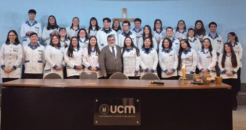 Un grupo de estudiantes de la Universidad Católica del Maule posando con un profesor en una ceremonia.