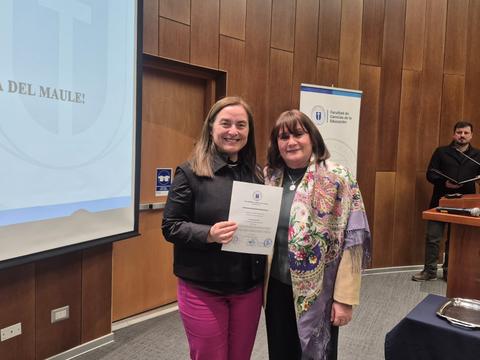 Dos mujeres sonrientes sosteniendo un certificado en un evento en la Universidad del Maule.