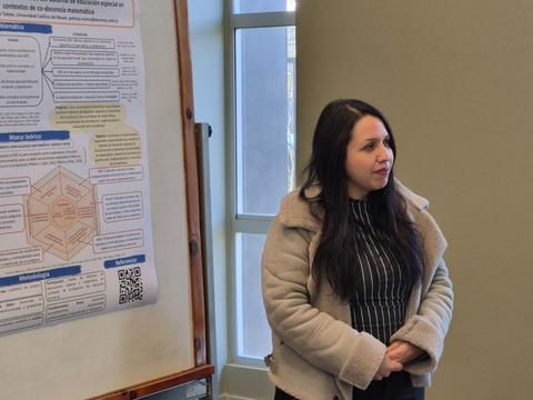 Una mujer de pie junto a un póster de presentación en un ambiente académico.