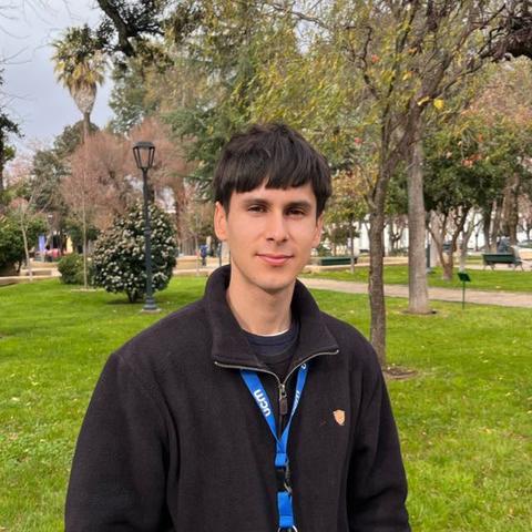 Un joven posando en un parque con árboles y un ambiente natural.