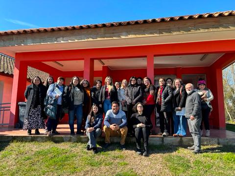 Un grupo grande de personas posando frente a un edificio de color rojo en un día soleado.