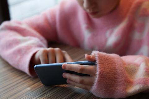 Un niño con un suéter rosado está usando un teléfono móvil.