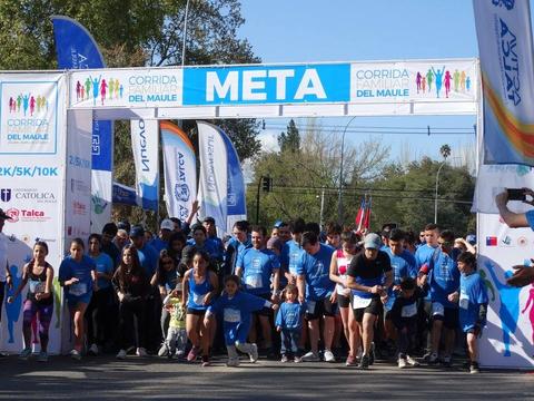 Una multitud de personas con camisetas azules está participando en una carrera bajo un arco de meta.