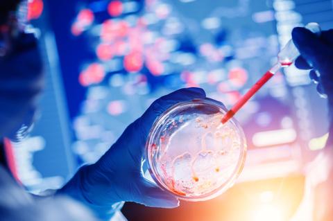 Una mano con guante sostiene un recipiente de laboratorio mientras se agrega un líquido con una pipeta, con un fondo de gráficos y datos científicos.