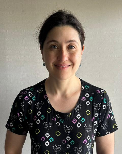 Una mujer sonriente que lleva una blusa colorida con un diseño moderno.