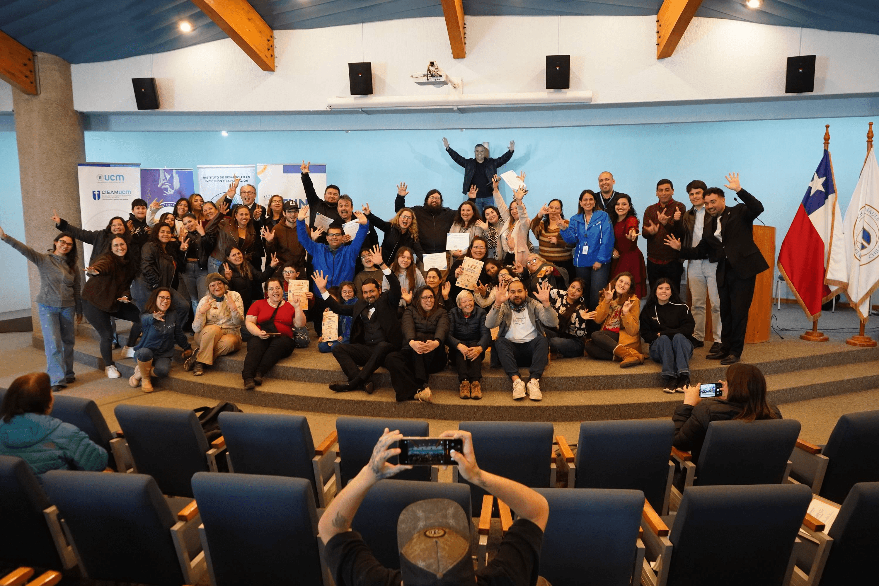 Un grupo grande de personas reunidas en una sala, celebrando y mostrando signos de alegría en un evento en Chile.