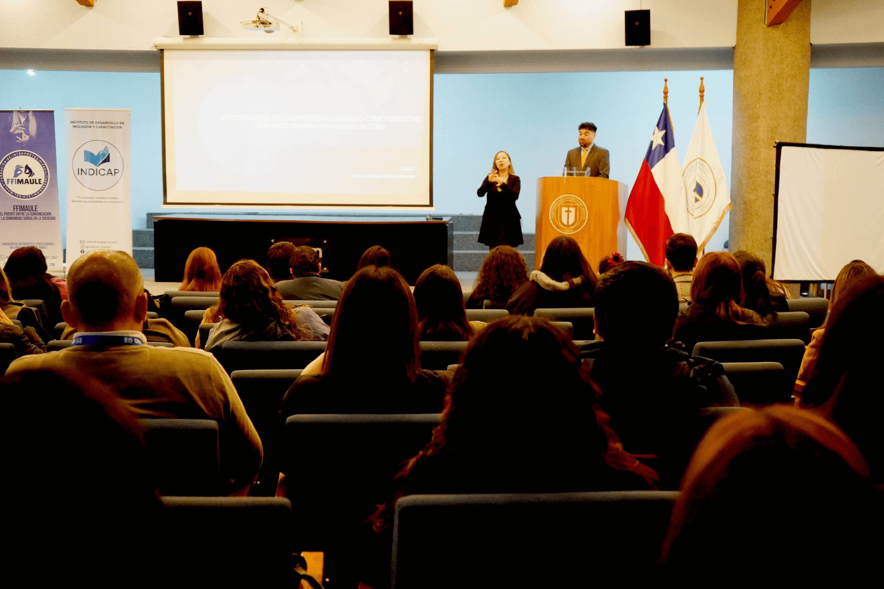 Una actividad académica en un auditorio con un presentador y una intérprete de lengua de señas.