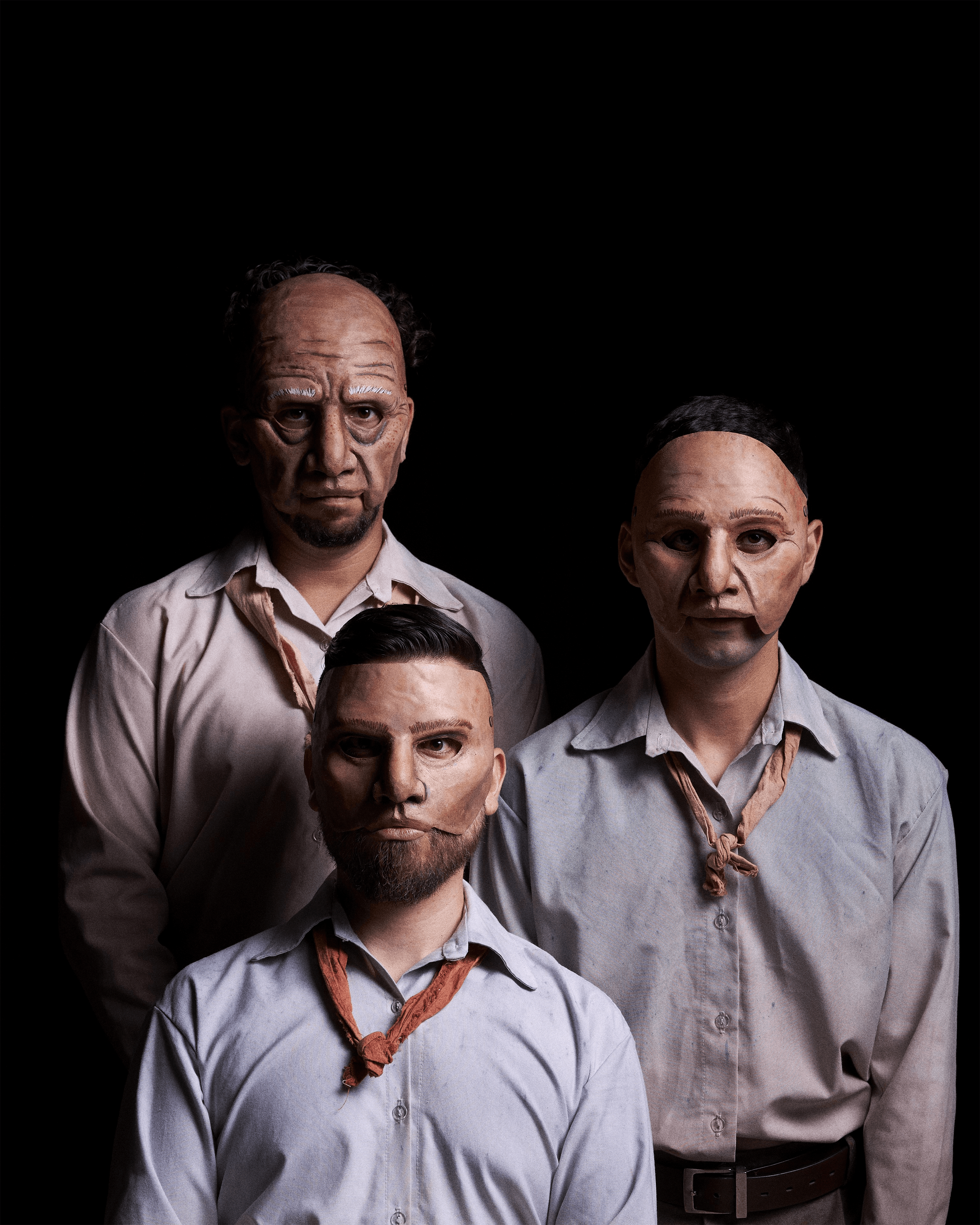 Tres hombres con maquillaje de máscaras en un fondo oscuro.
