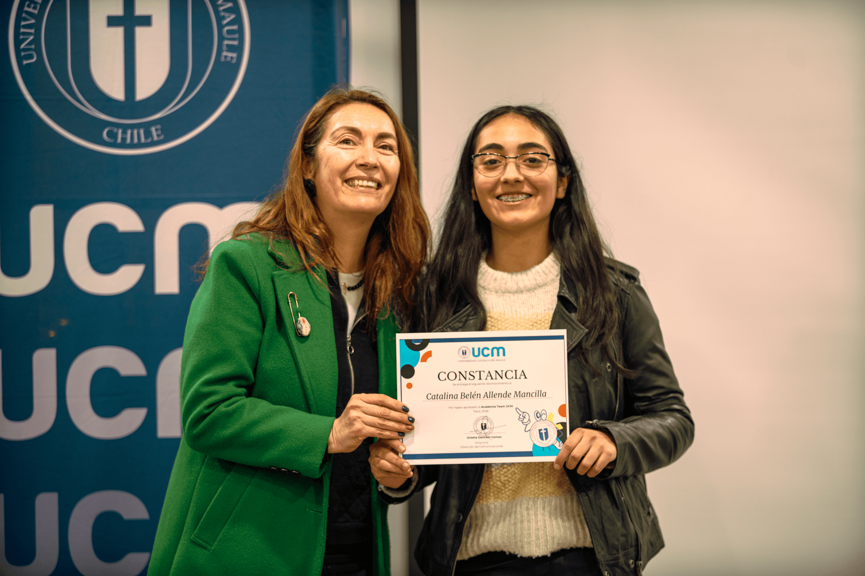Dos mujeres sonrientes posan con un certificado en un evento de la universidad.