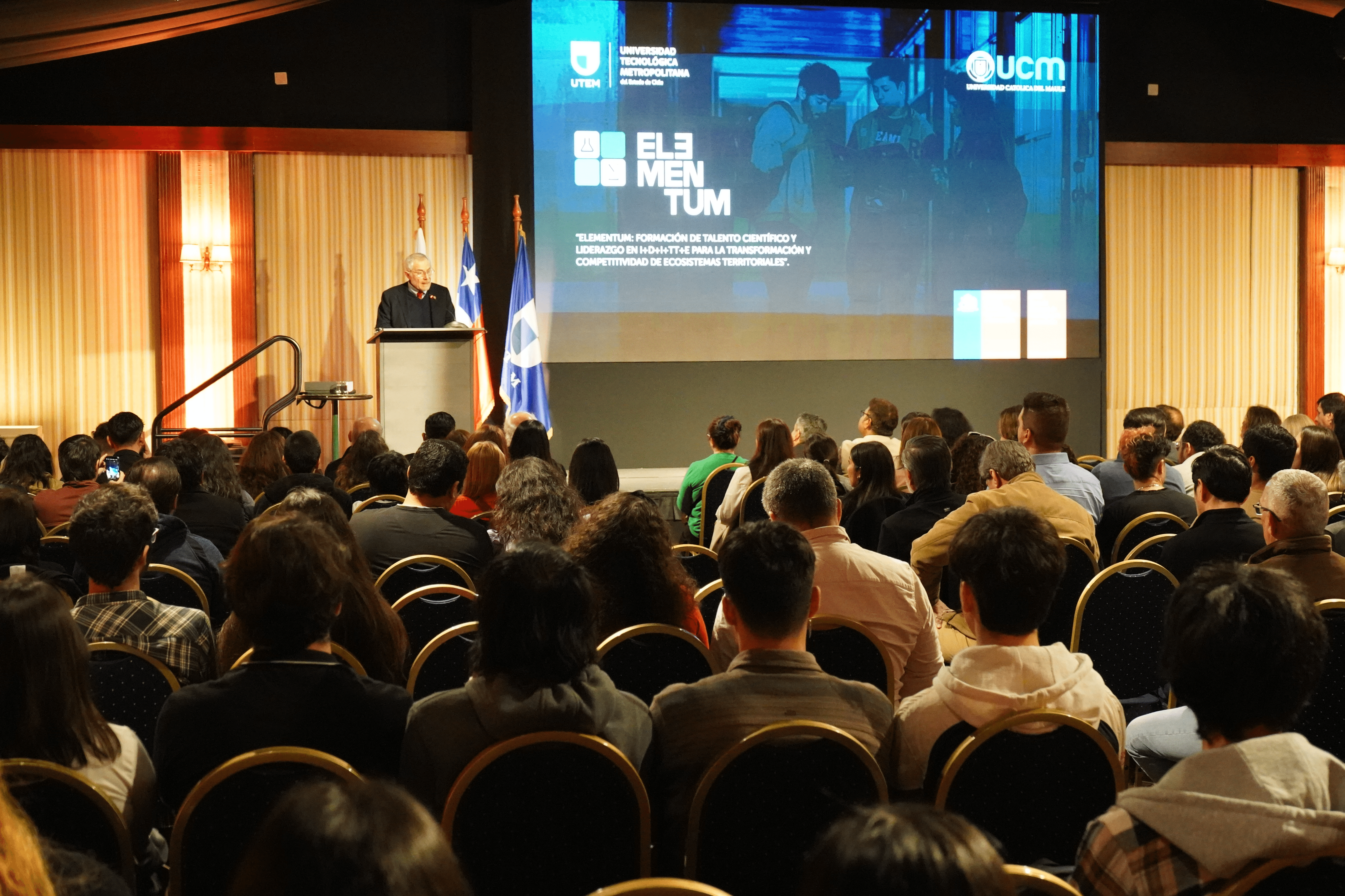 Un evento académico con un gran público escuchando a un orador en el escenario.
