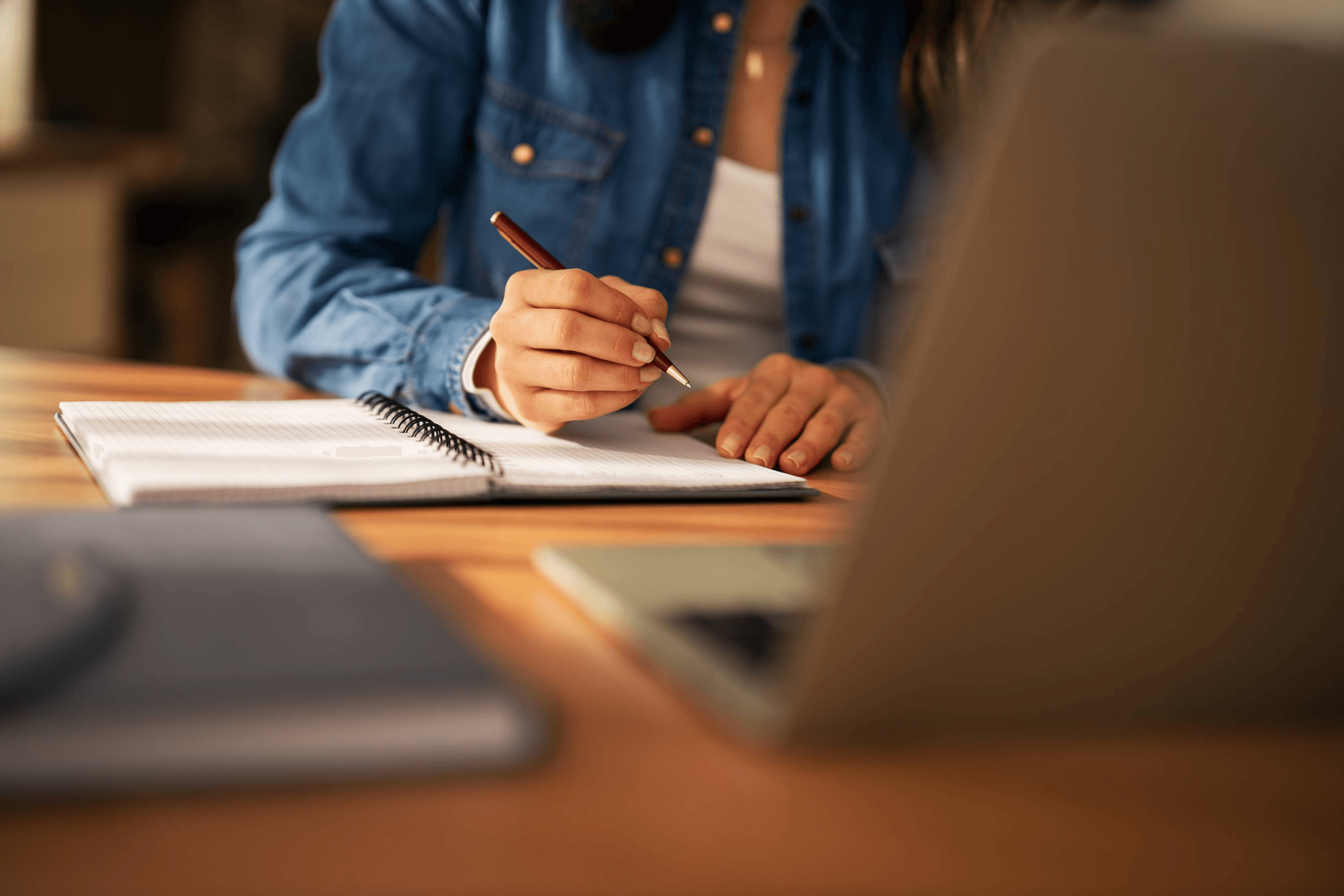 Una persona está escribiendo en un cuaderno mientras trabaja en su computador.