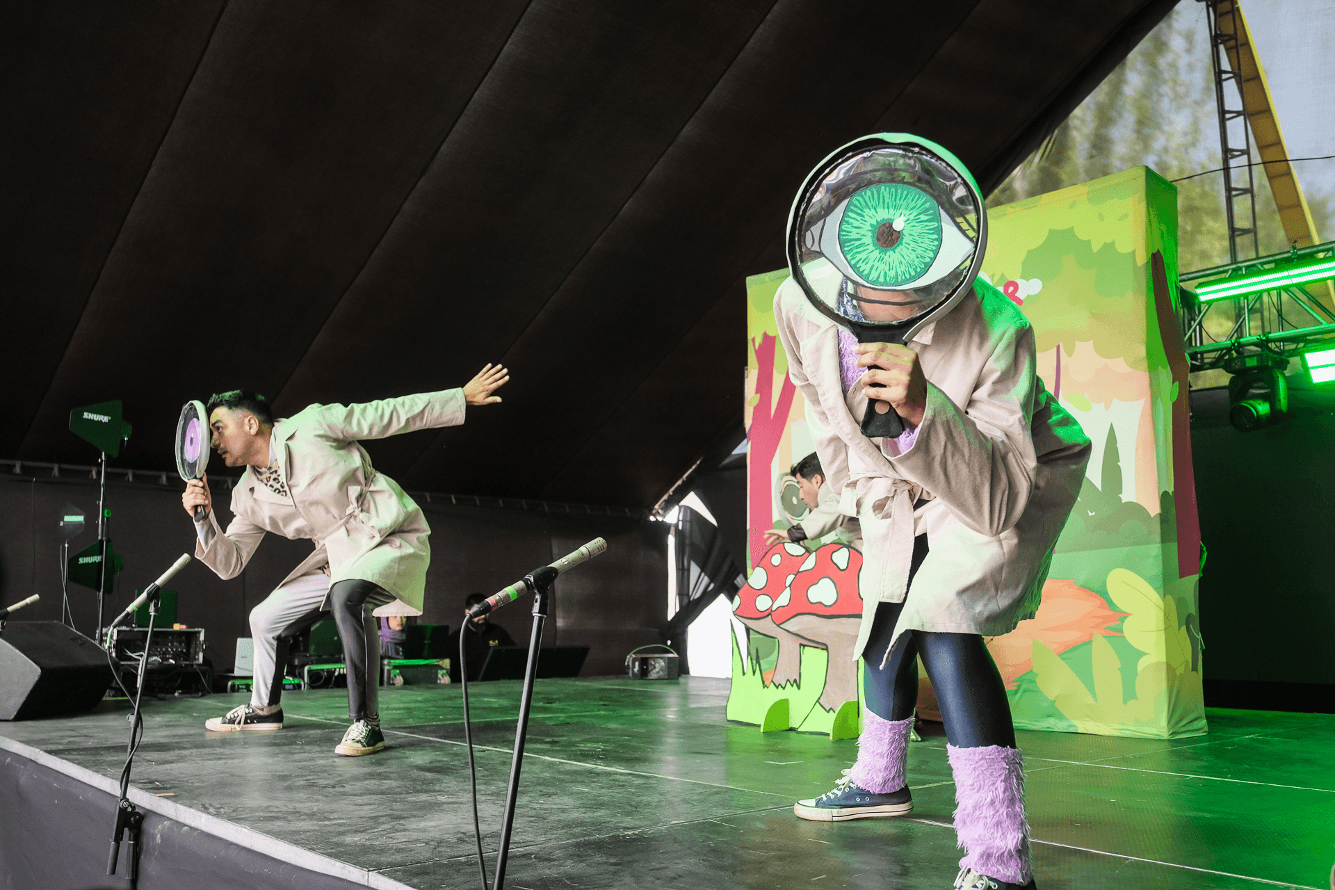 Dos personas en un escenario realizan una actuación divertida con grandes lentes y un fondo colorido.