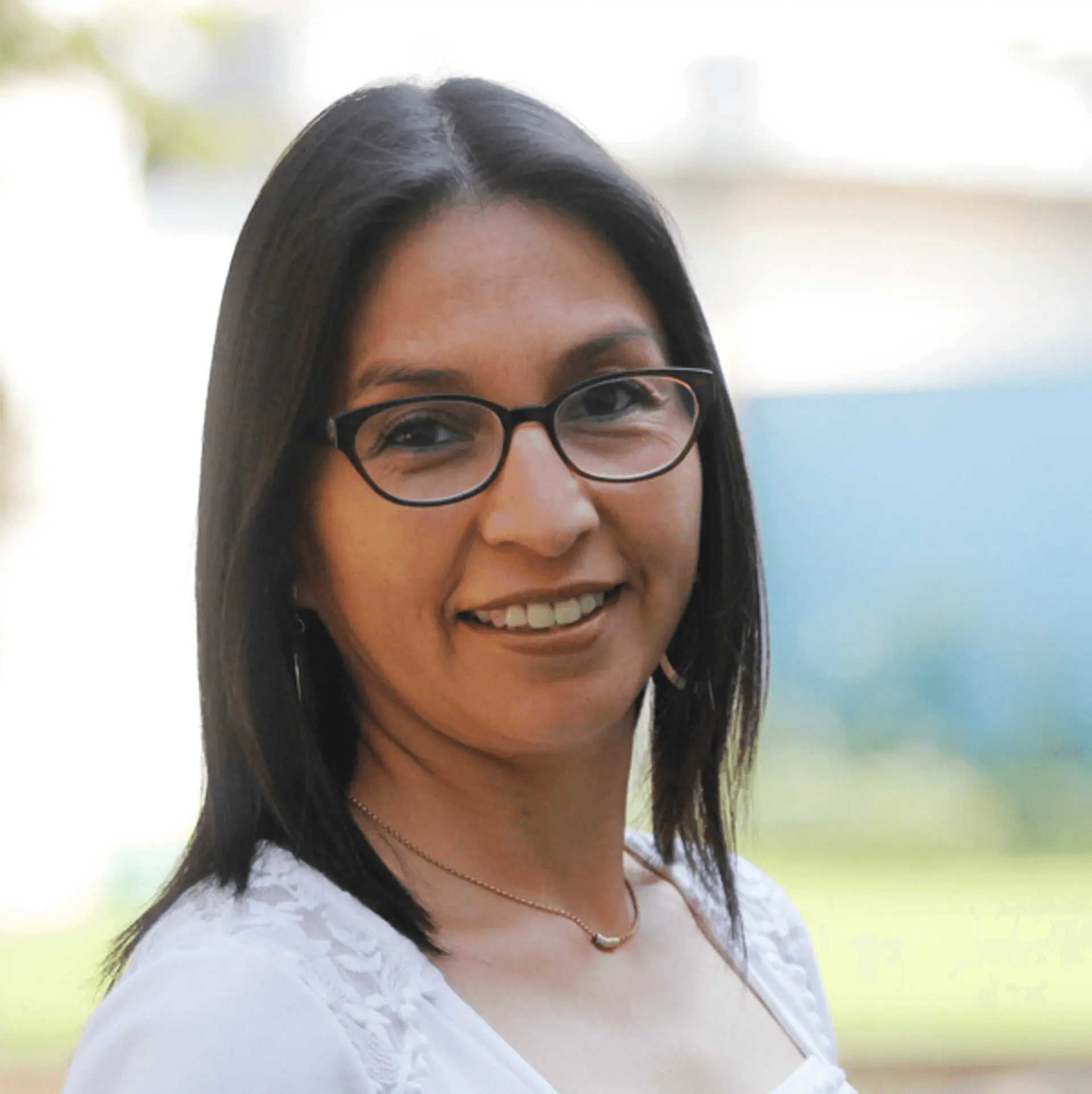Mujer sonriente con gafas en un fondo difuso.