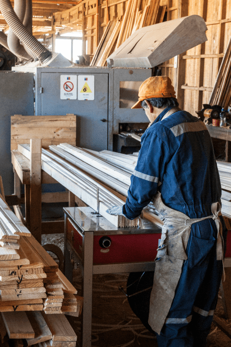 Un trabajador en una maderería procesando tablas de madera con una máquina.