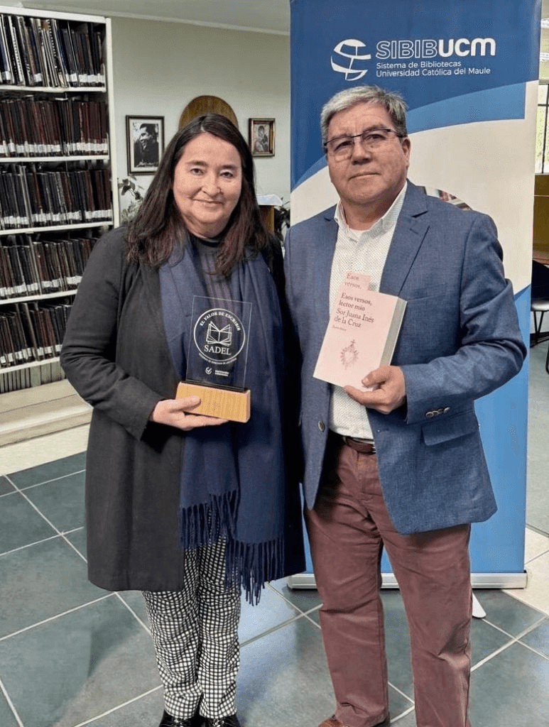 Una mujer y un hombre posan juntos en una biblioteca, sosteniendo premios y libros.