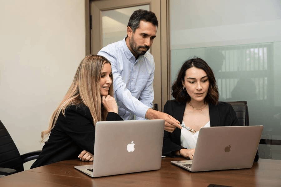 Tres personas en una reunión están trabajando en sus computadores portátiles.