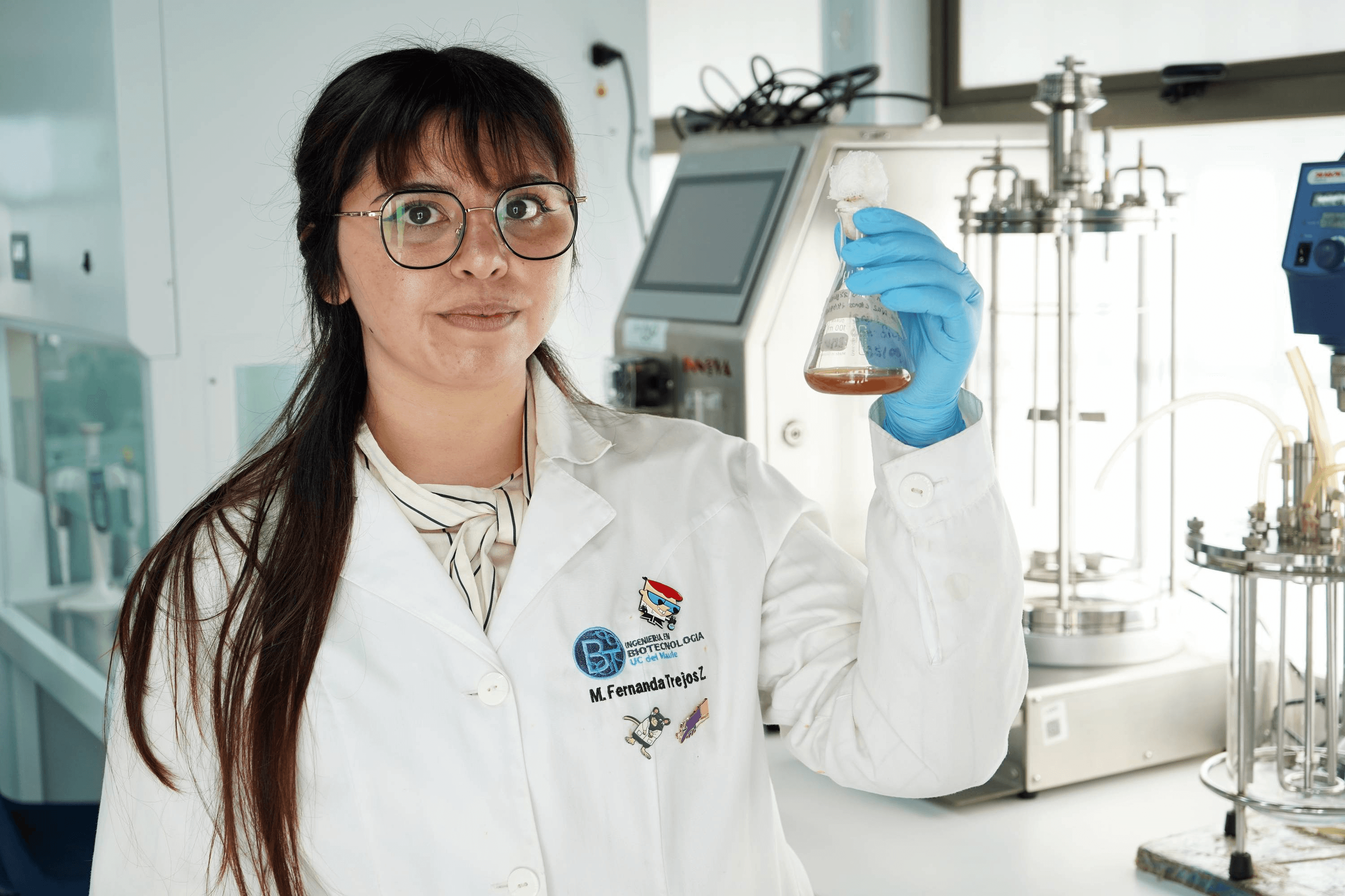 Una científica chilena muestra orgullosa un matraz en un laboratorio moderno.
